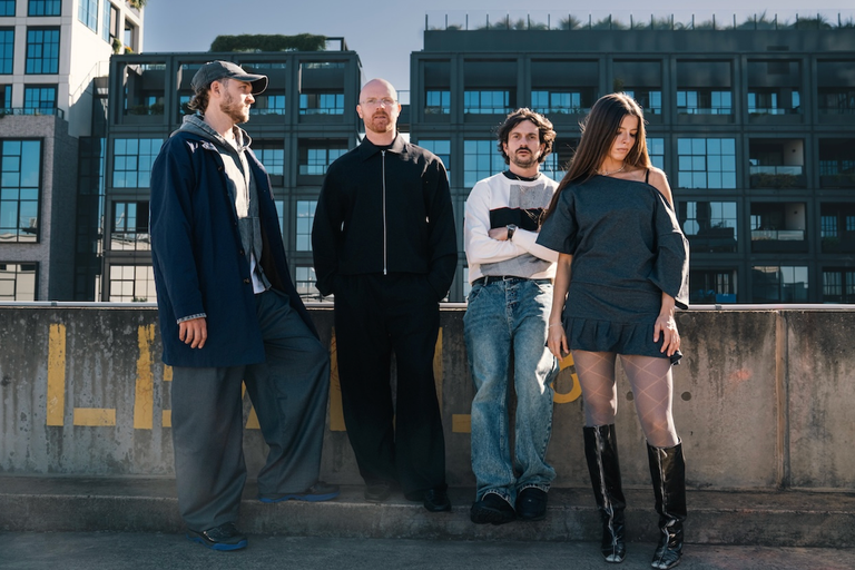 Australian indie rock band The Jungle Giants stand outdoors against modern apartment buildings in stylish streetwear and dark outfits.
